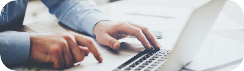 Close-up of a person’s hands typing on a laptop keyboard, with documents on the desk nearby.