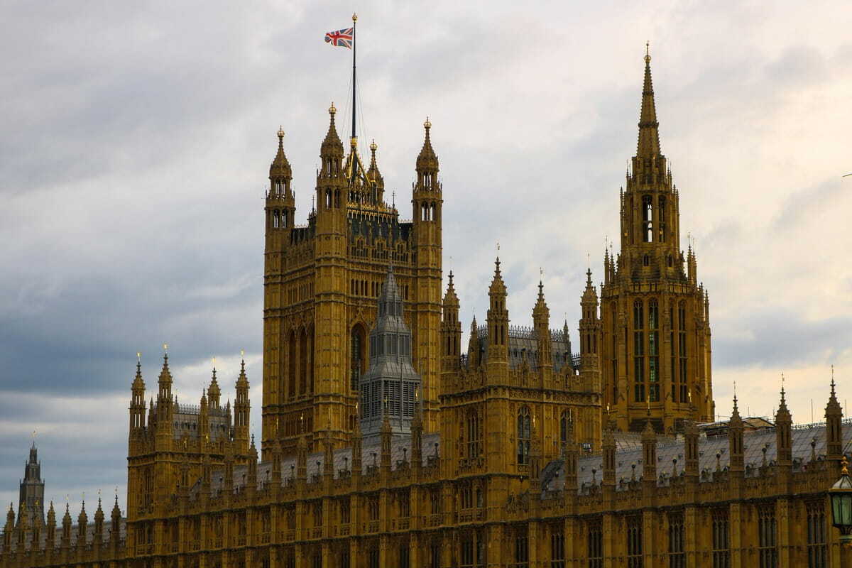 A photograph looking upwards captures the elaborate facade of the Palace of Westminster in London on a heavily overcast day.