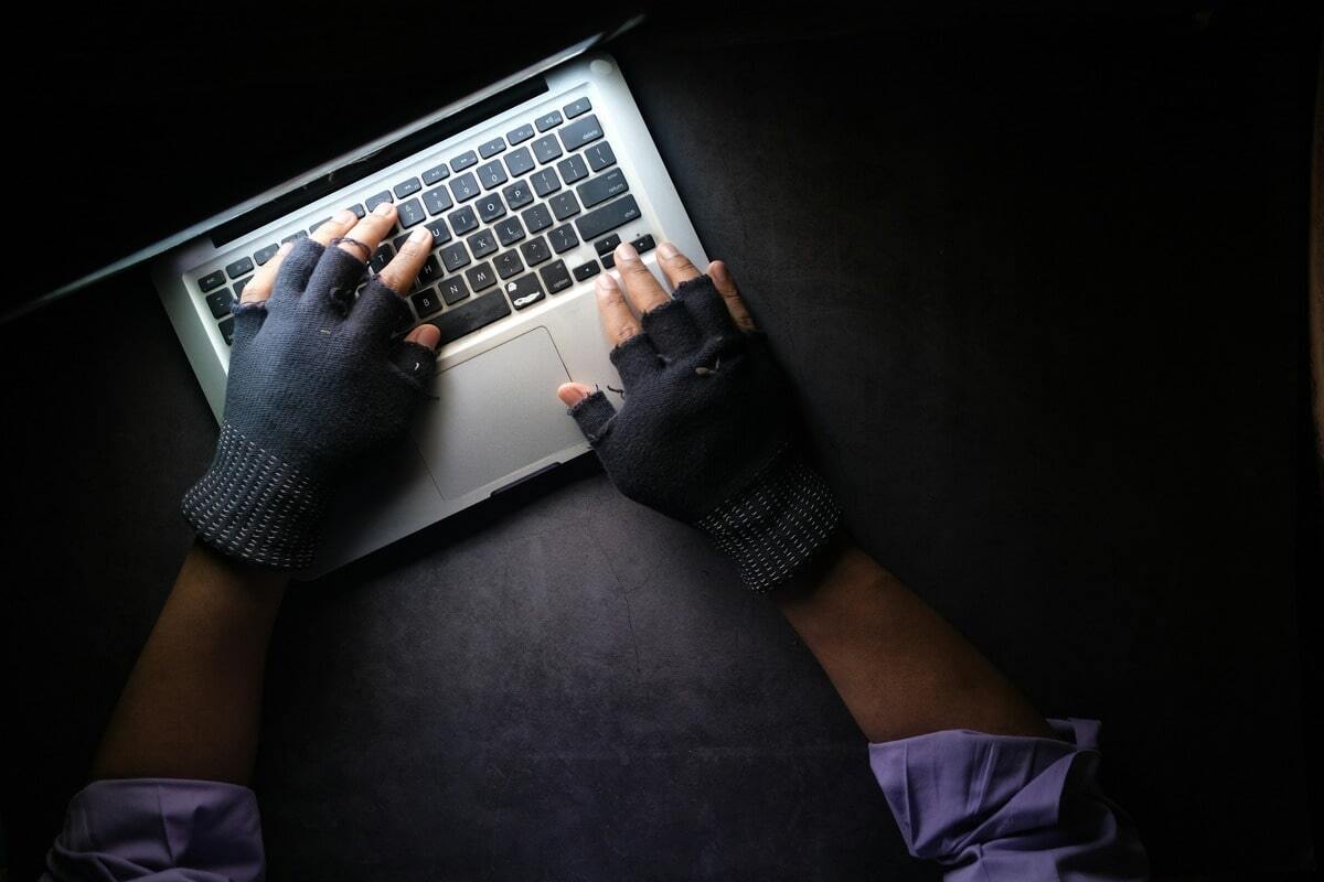 Person wearing fingerless gloves typing on a laptop in a dimly lit setting, symbolising identity and tenancy fraud.