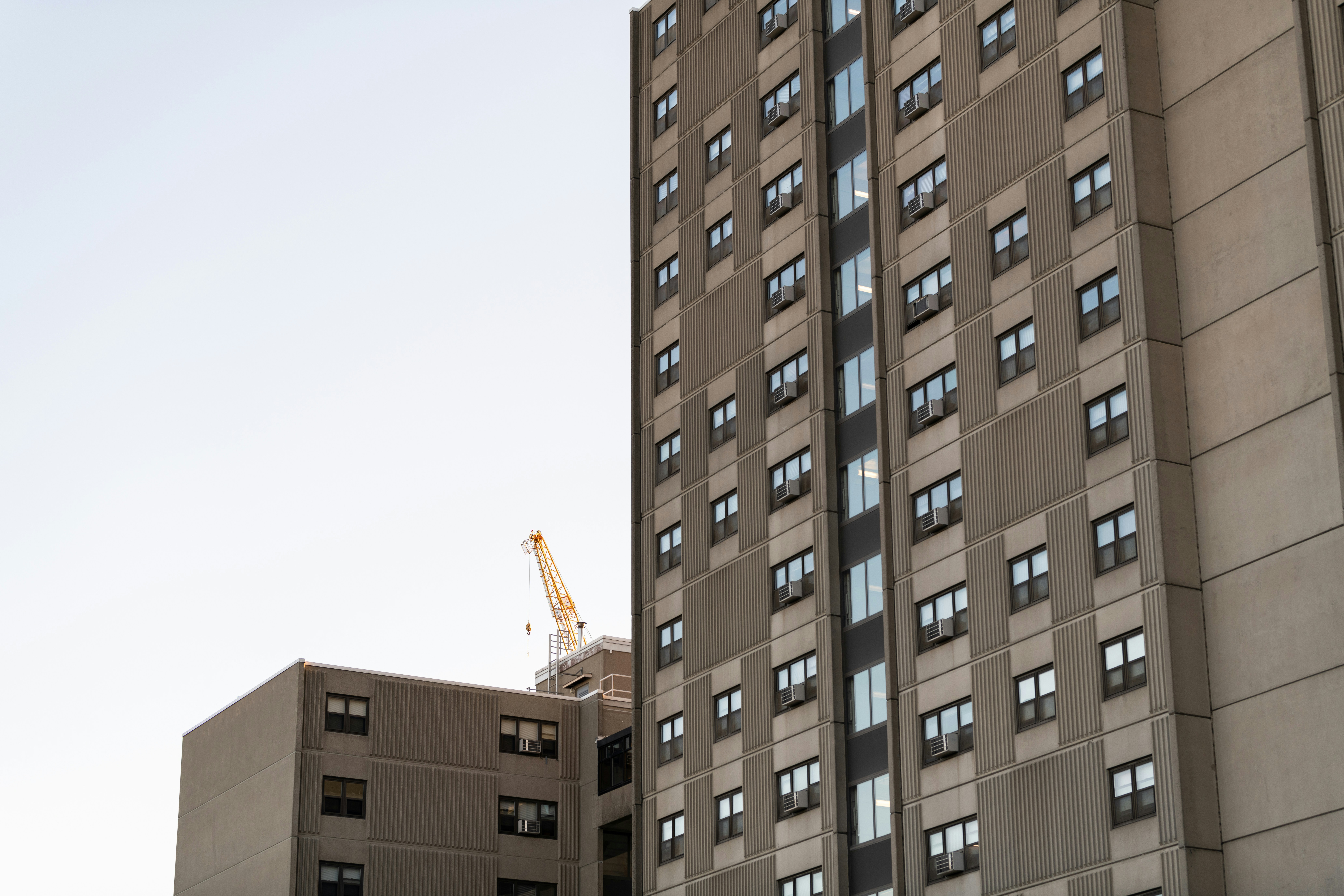 Daytime shot of a block of brutalist high-rise flats with a yellow crane in the background. 