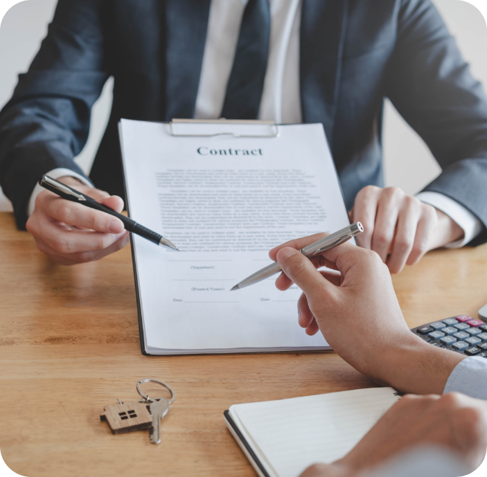 Two people in business attire reviewing and signing a contract at a desk, with pens in hand, keys, notebook, and calculator nearby.