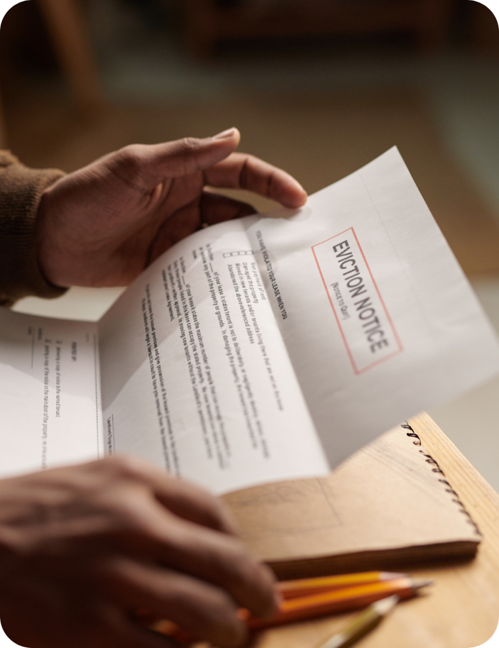 Person holding and reading a printed eviction notice at a table with a notebook and pencils nearby.