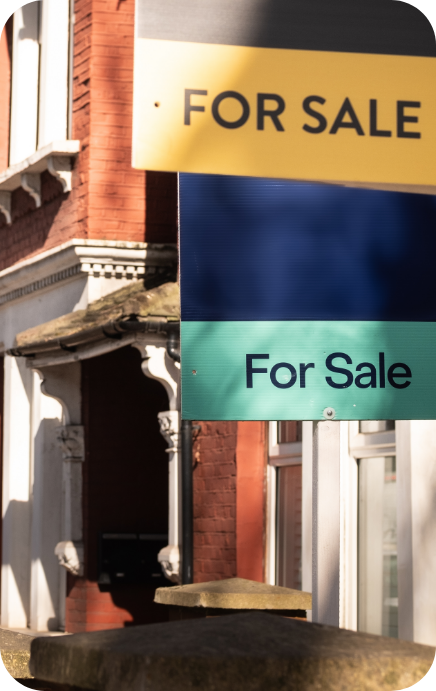 House exterior with multiple ‘For Sale’ signs displayed outside, in front of a brick building.